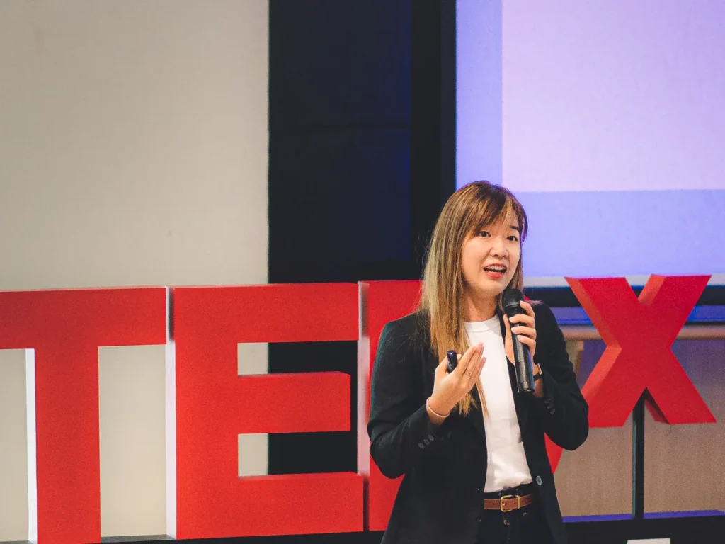 Yin Sinn speaking into a microphone on the TEDxUTM stage