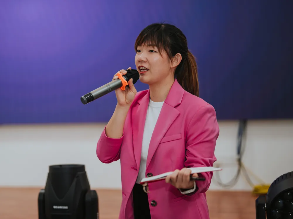 Yin Sinn in a pink blazer speaking into a microphone during a corporate training session