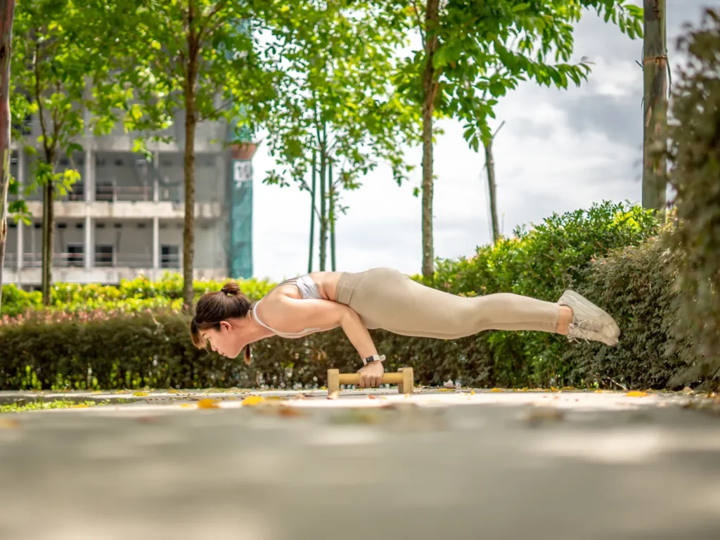 Yin Sinn holding a calisthenics planche on parallettes in a park